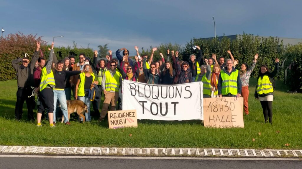 Une trentaine de personnes avec un gilet jaune posent autour d'une banderole ou il est inscrit "bloquons tout"